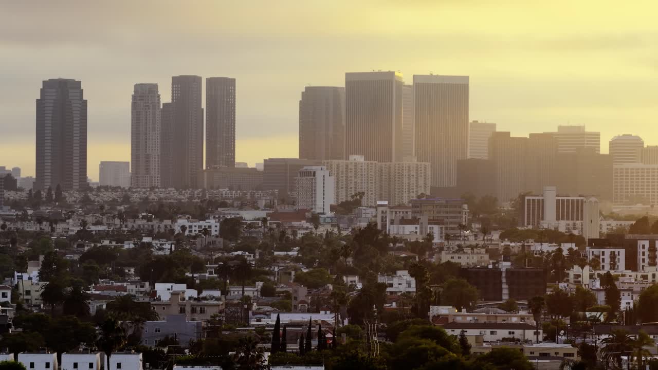 Vista aerea con teleobiettivo di Los Angeles che mostra lo skyline di Century City con torri gemelle, primo piano residenziale con palme, illuminazione dell'ora d'oro, forte foschia atmosferica, cielo giallo caldo, a strati