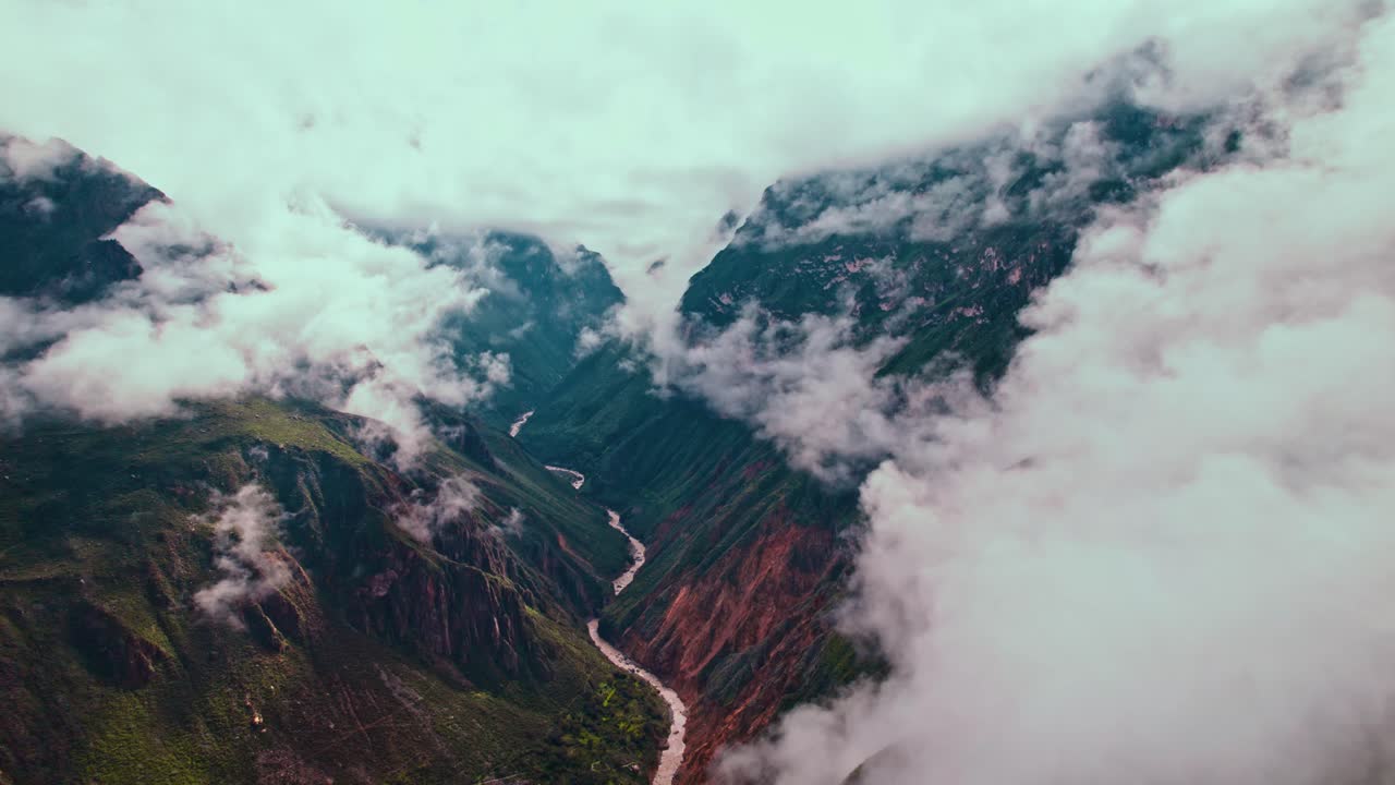 Aerial drone flight backward reveals Colca Canyon's vastness, post-rain clouds, lush greenery, and Colca River