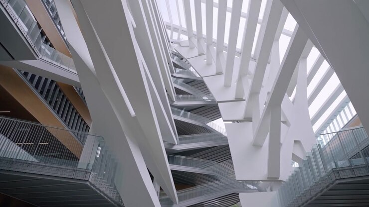 Un movimiento de cámara ascendente revela más de un techo acristalado brillante sobre un interior multinivel, enmarcado por soportes blancos que se cruzan, pasarelas metálicas, barandillas transparentes y paneles de pared cálidos.