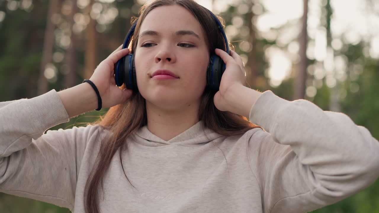 여성은 공원에서 헤드폰으로 음악을 즐긴다. 젊은 여자는 여름 해가 지는 나무에 둘러싸인 좋아하는 노래의 리으로 자연에서 즐거움을 얻는다.