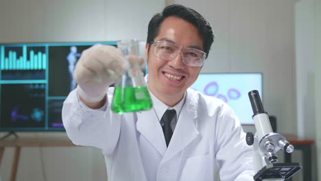 young asian male research scientist looking  glass test tube and warmly smiles into the camera