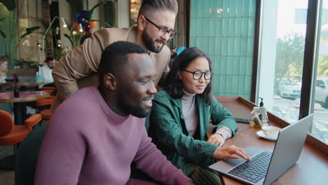 multiethnic colleagues using laptop and discussing project in cafe