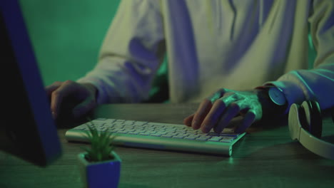 hands of a male worker typing on the keyboard working with a computer on a green colorful background. close-up.