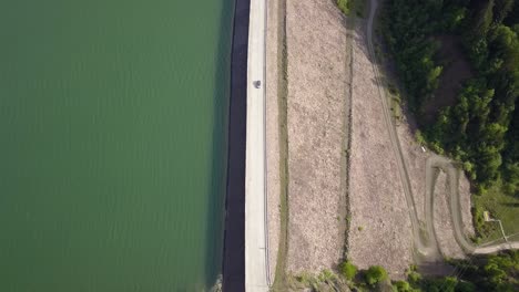 Aerial-Top-down-Show-of-road-splitting-water-and-landscape-with-car-driving-in-the-middle