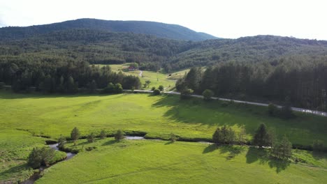 drone shot of secluded house in idyllic mountain landscape, creek pine forest meadows and road