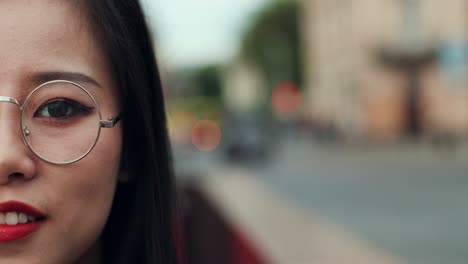 close up of the half face of the young pretty woman in glasses smiling cheerfully and looking straight to the camera outside