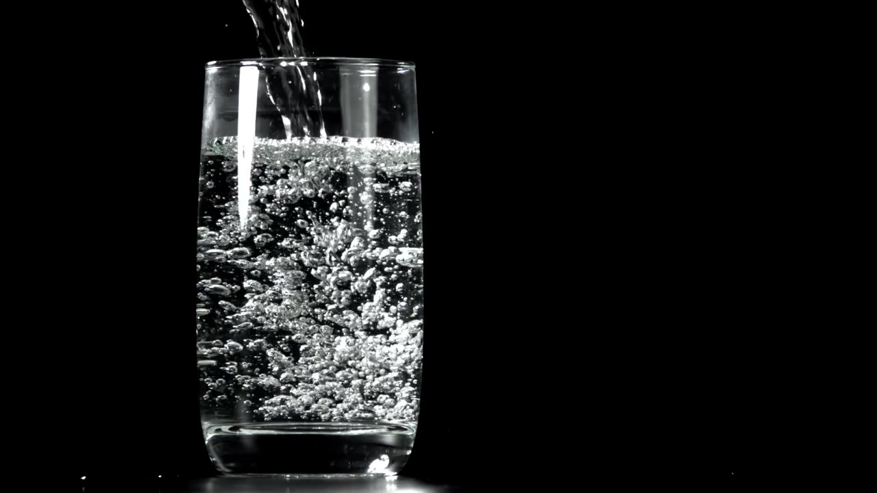 Acqua trasparente versata in un bicchiere con bollicine su sfondo nero