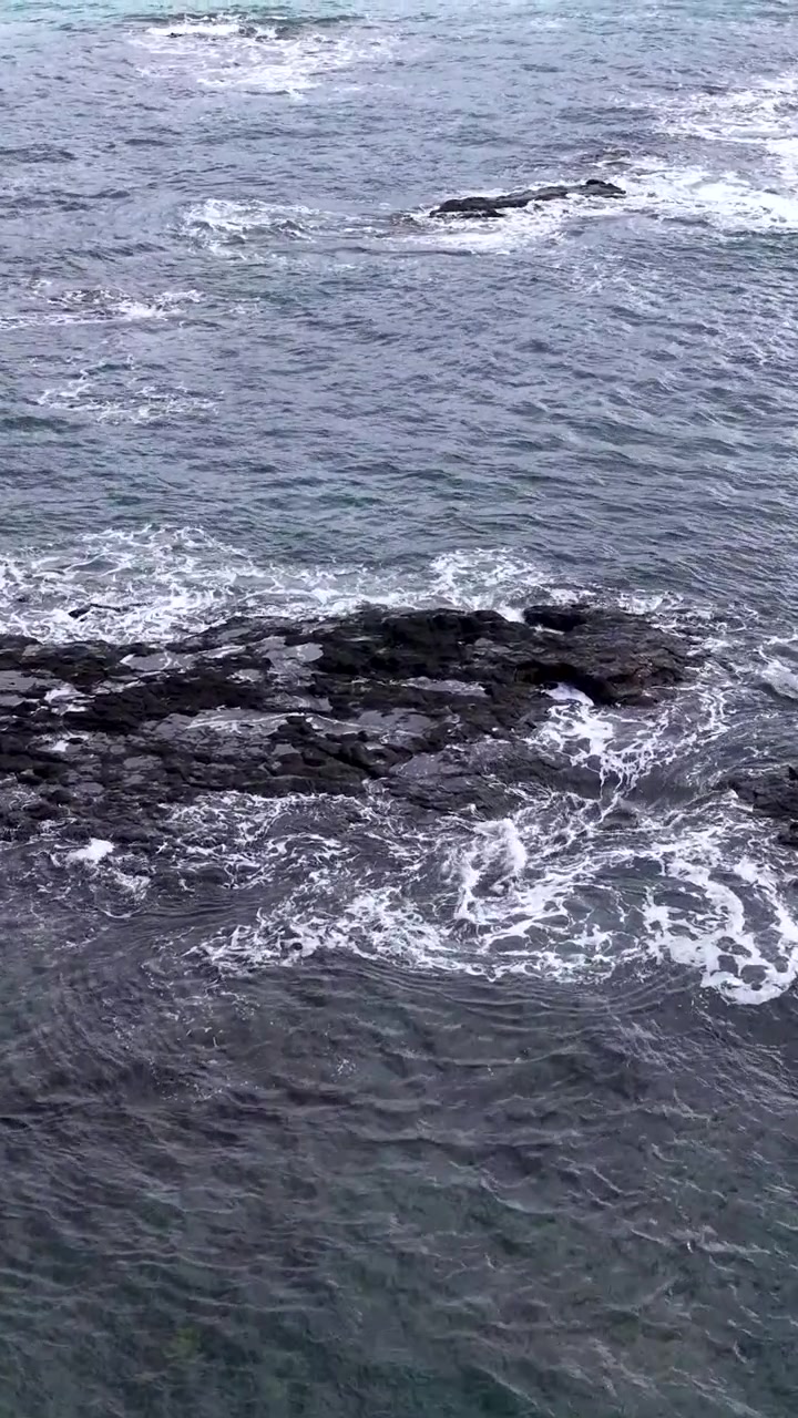 Pengambilan gambar sudut tinggi air laut pirus yang membasahi bebatuan karang gelap di Australia.
