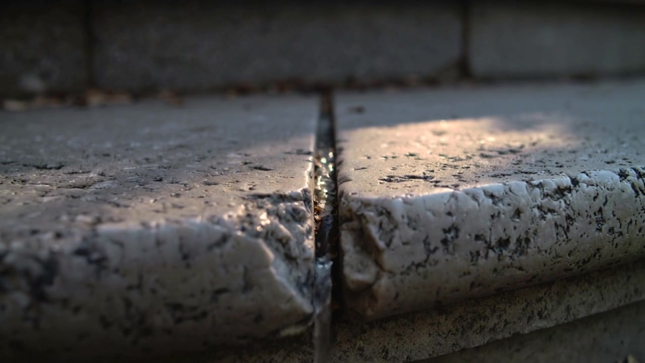 Fessura scintillante che cattura il sole sulle lastre, la gravità che trascina l'acqua in un rivolo oltre il bordo del cornicione del cortile.