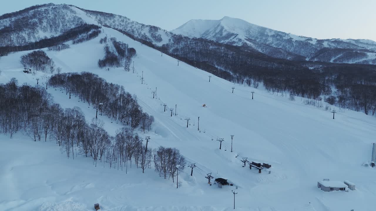 Statyczne ujęcie ratraka przygotowującego otwarte trasy na stoku narciarskim poza trasami przed godzinami otwarcia na Hokkaido, Japonia