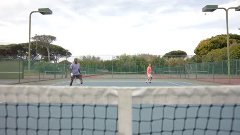 Two-diverse-male-friends-playing-doubles-returning-ball-over-net-at-outdoor-court-in-slow-motion