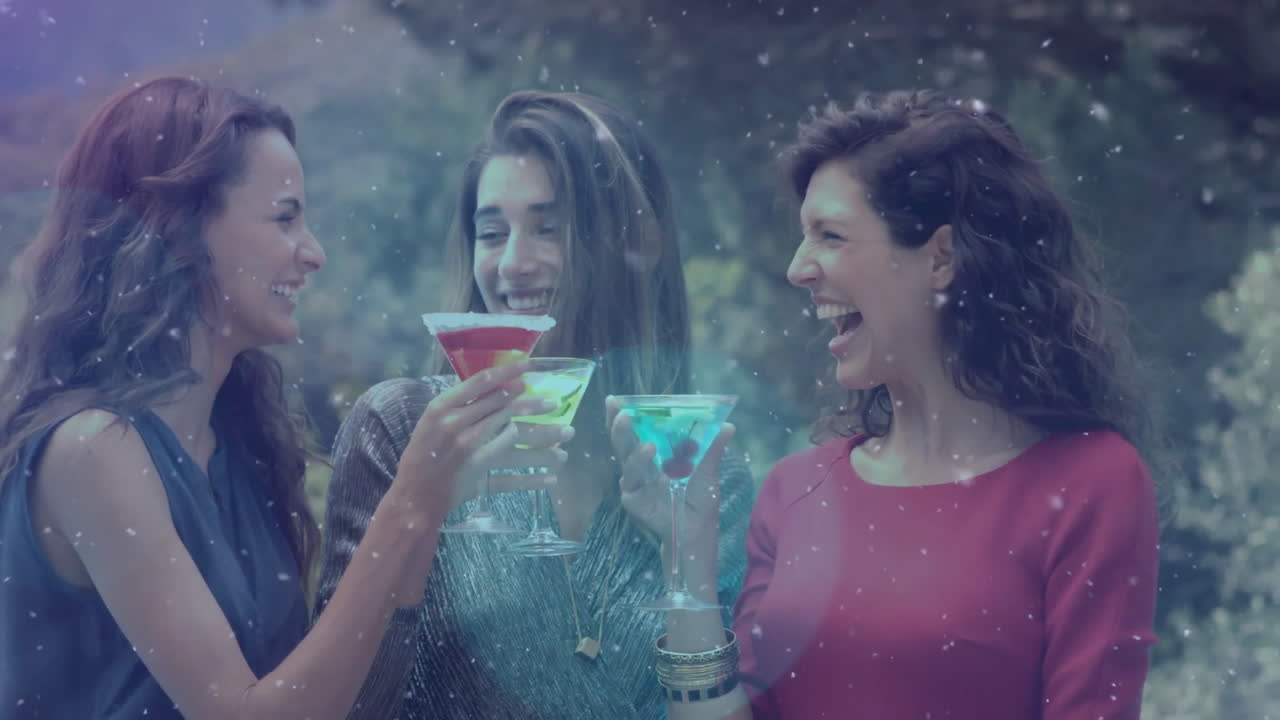 Snowfall animation over women clinking colorful cocktails and laughing outdoors