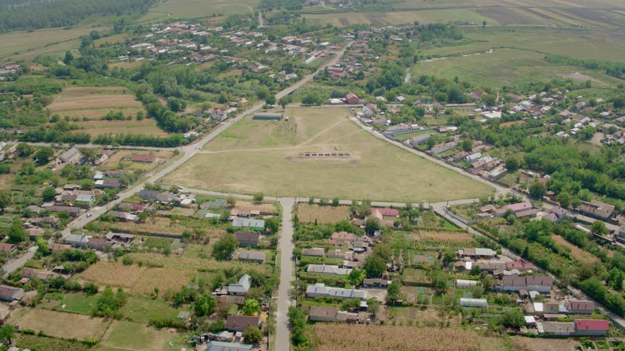 Drone footage showing an expansive aerial view of The archaeological site in Romanian village of Dobrosloveni. Houses and farmland surround a large, distinct triangular central field