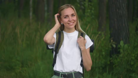 portrait of a young woman traveler in the sun looking directly into the camera and smiling flirting traveler with a backpack in the park and in the woods in slow motion