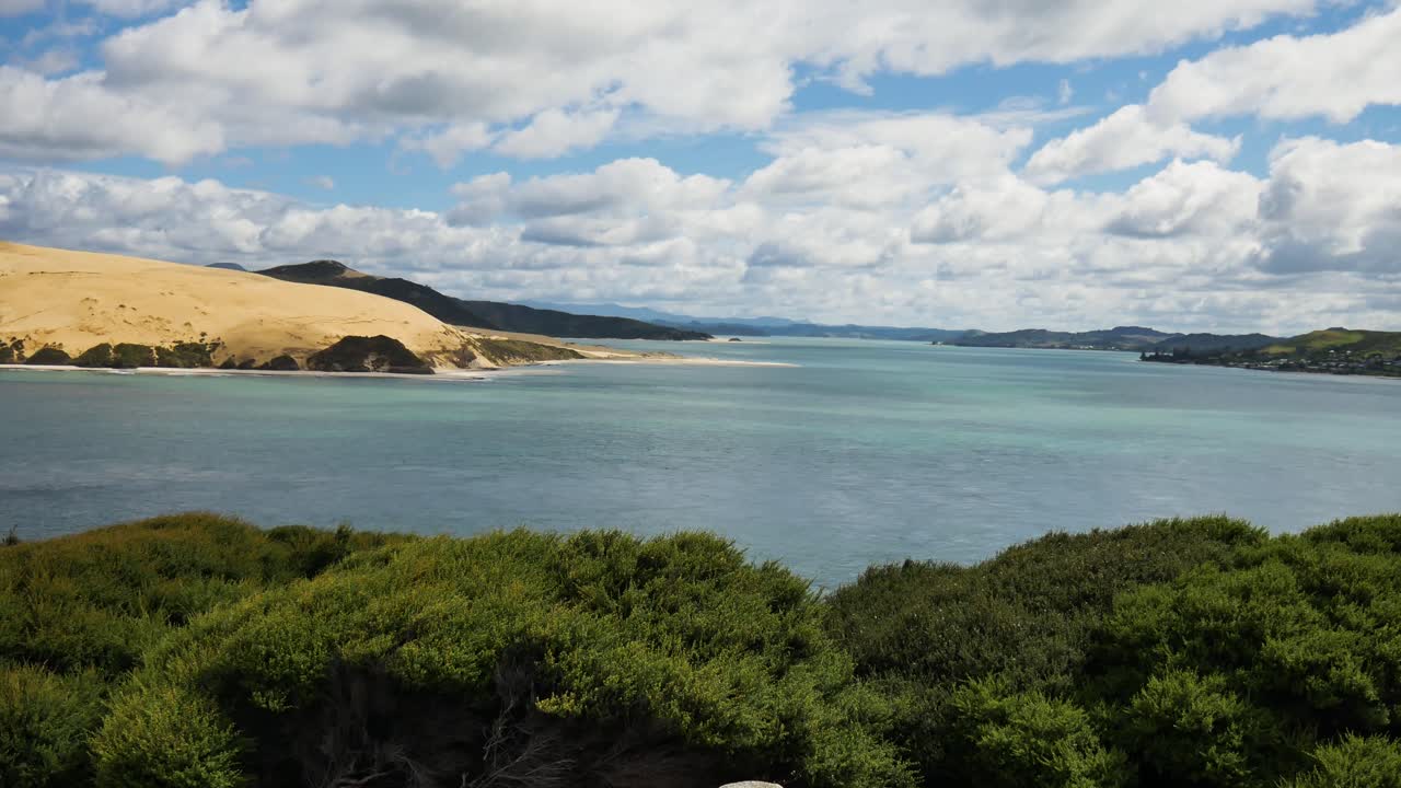 Dolly forward shot of beautiful Kauri Coastline with bush, clear ocean water and sandy mountains during cloudy day