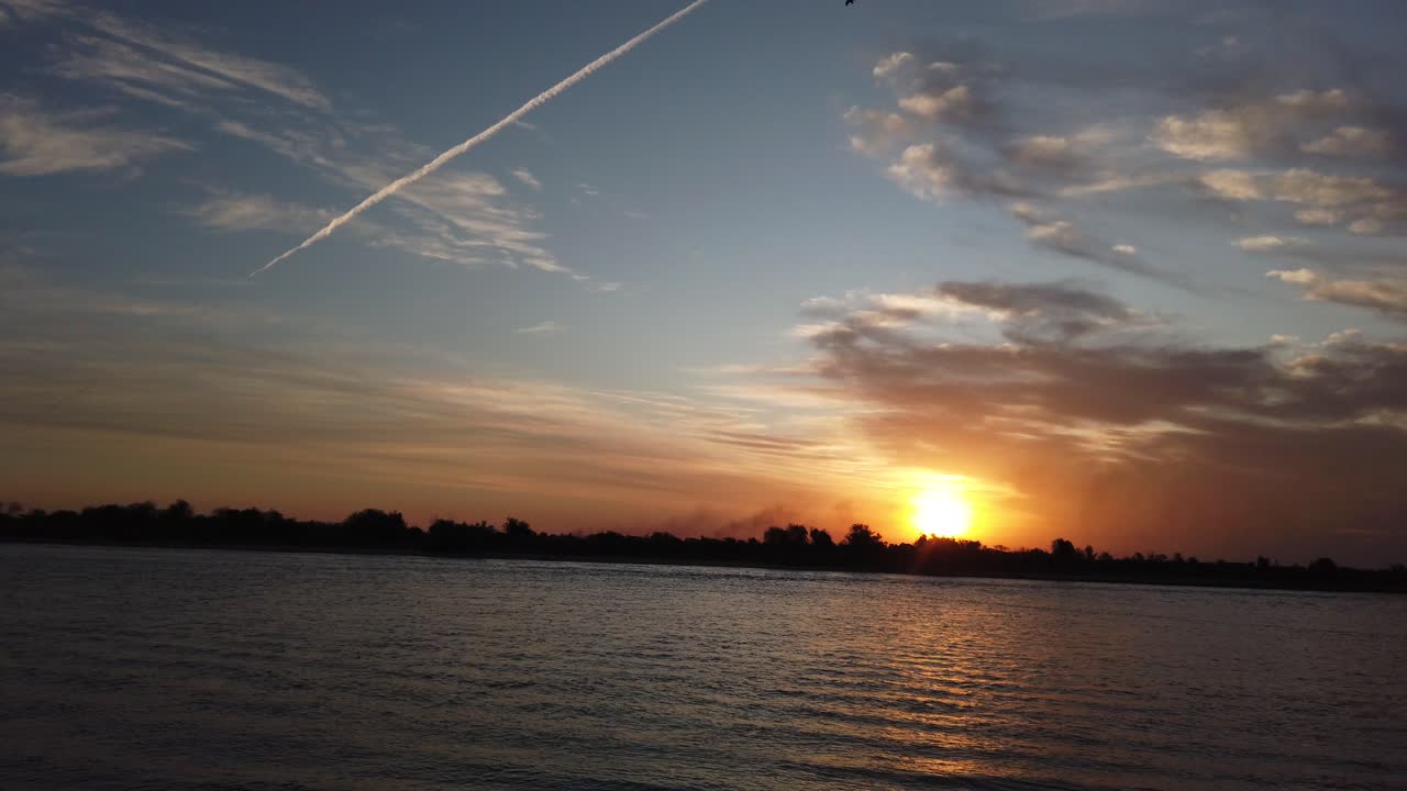 해가 지는 동안 다채로운 하늘에서 화학적 흔적과 함께 공중 해경, 멀리서 실루으로 도시 풍경, 음모 이론