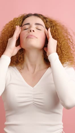young woman suffering from headache on pink background
