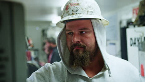 caucasian man wearing protective helmet and hoodie stands at the wagon with oil drilling equipment. bearded worker operating the machines controlling oil production.