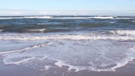 low angle shot of waves splashing on sandy shore during sunny day with horizon in background