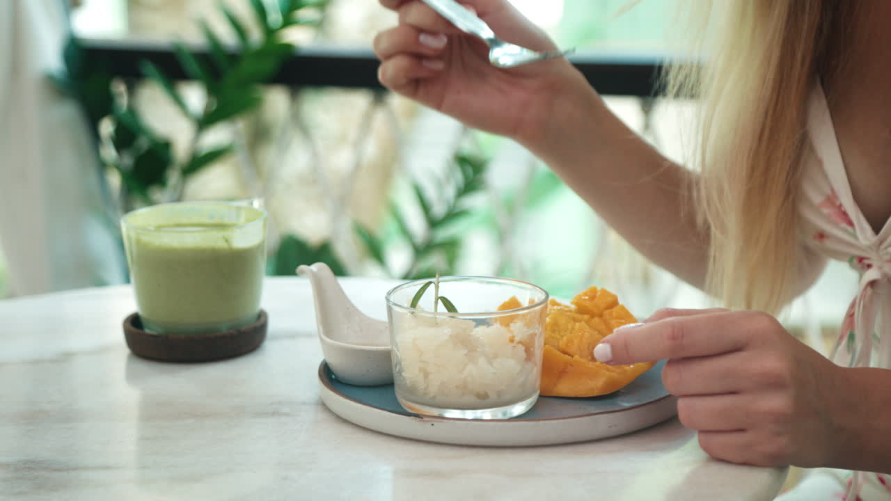 Woman enjoying Thai dessert with mango and sticky rice at a cafe