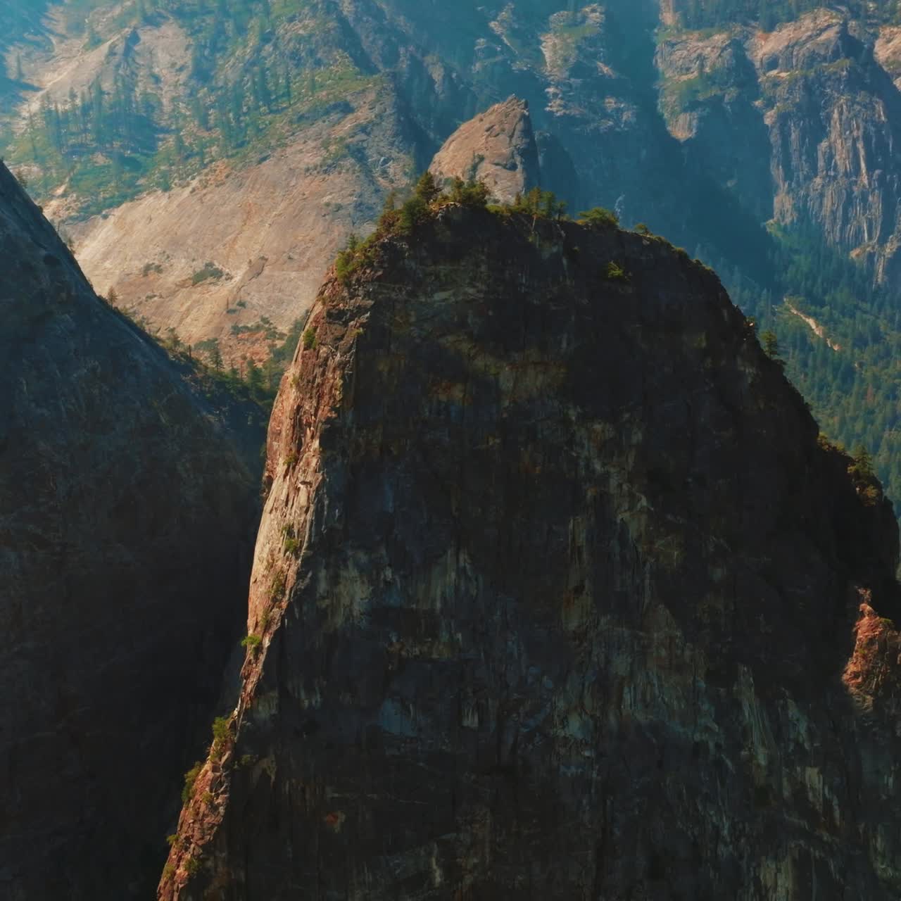 Craggy steep cliffs of Yosemite National Park, California, USA on sunny day. Rare pine trees growing on tops of mountains and thick woods at the foot. Top view