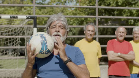 happy senior football player tossing and catching ball while looking at the camera on the soccer field