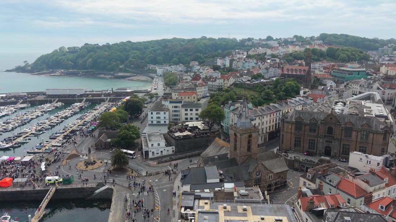 Volo in avanti sul Canale di St Peter Port Guernsey, sulla città e su Albert Marina verso la Baia di Havelet, con uno scorcio dei festeggiamenti sul Molo Albert in una soleggiata Giornata della Liberazione