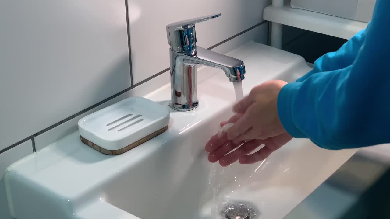 foto lateral de una mujer lavándose las manos con jabón debajo del grifo del lavabo del baño.
