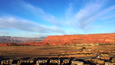 view from a drone of a sunlit city and a road with cars in the foreground and red mountains on the horizon