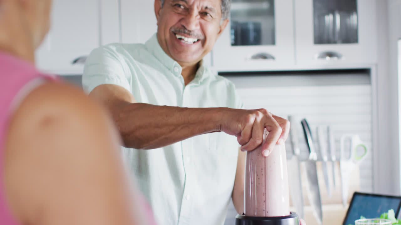 una feliz pareja biracial está preparando una bebida saludable en la cocina.