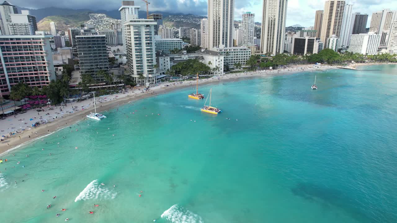 Splendida ripresa aerea rotante in 4K con drone di Waikiki Beach mentre le barche da crociera per la cena al tramonto attraccano sulla spiaggia per prelevare coppie che desiderano gustare bevande e cena, mentre le famiglie si godono le loro vacanze.