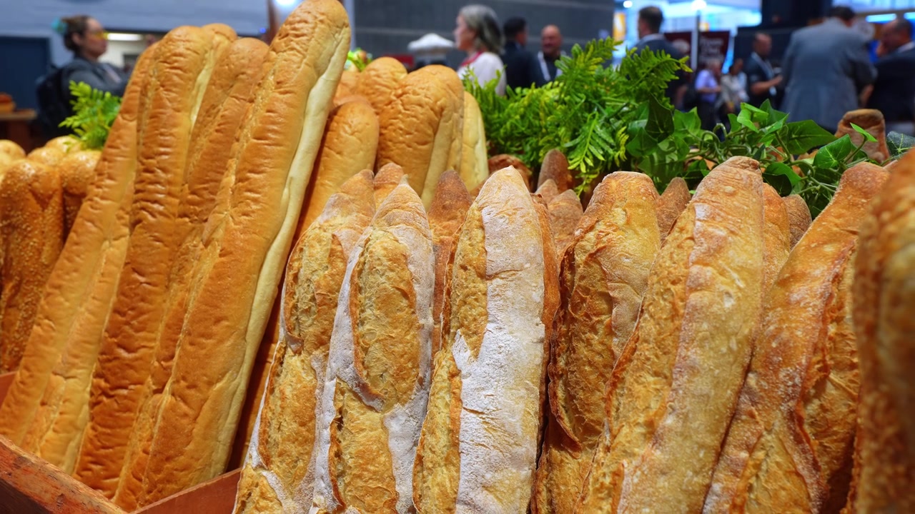 File di baguette dorate esposte in verticale a una mostra gastronomica. Primo piano di pagnotte di pane francese croccanti con guarnizione di felce verde.