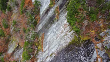 Approaching-a-mountain-rock-face-covered-in-decaying-foliage-and-trees-on-Mount-Washington,-Hampshire,-USA