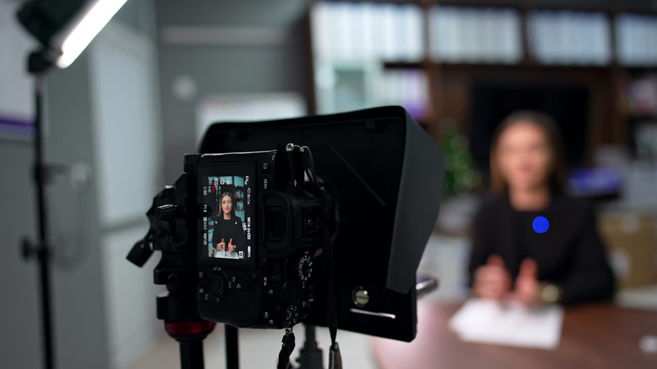 Serious brunette blogger recording a video content. Professional camera filming a speech. Blurred backdrop.