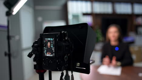 serious brunette blogger recording a video content. professional camera filming a speech. blurred backdrop.