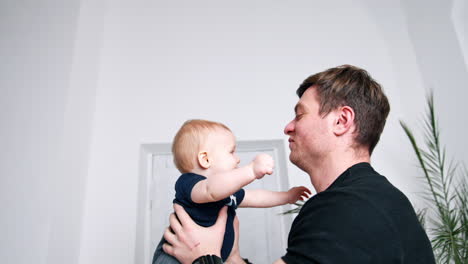dark-haired man tossing up a cute happy infant. blonde woman stands watching at backdrop.