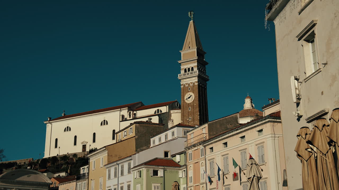 Vista cinematografica di Pirano, Slovenia, che mostra la chiesa di San Giorgio e un edificio in stile veneziano di fronte. Il filmato cattura l'architettura storica, i tetti e l'affascinante città costiera.
