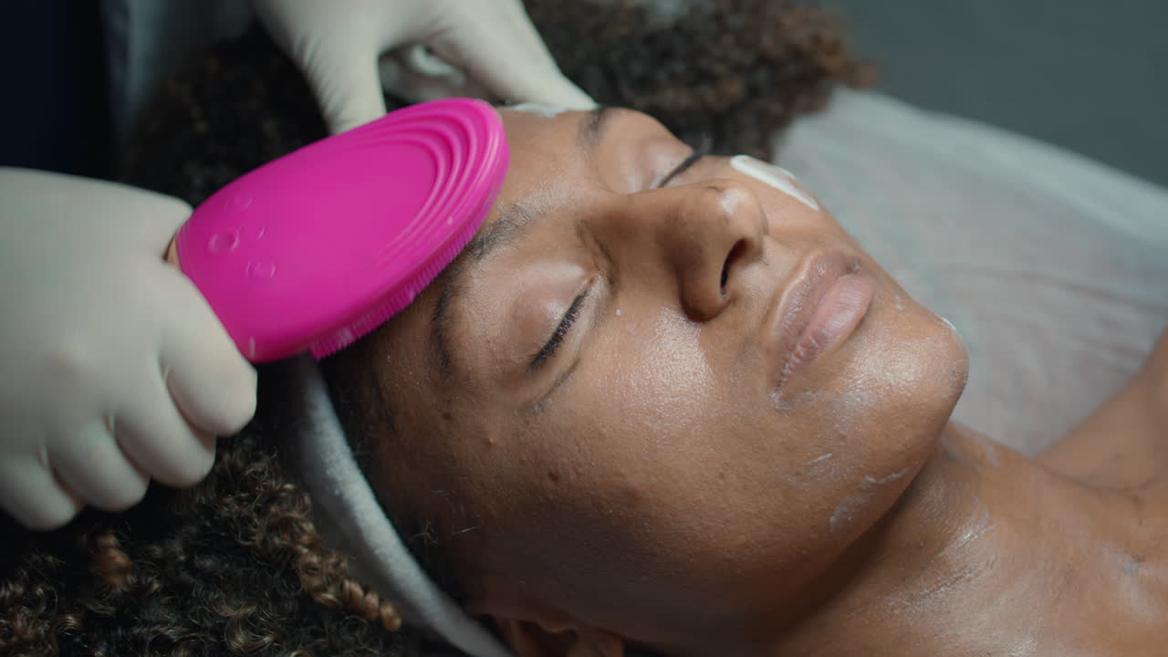 Gros plan de mains appliquant de la crème pour le visage avec un pinceau. Esthéticienne massant une cliente.