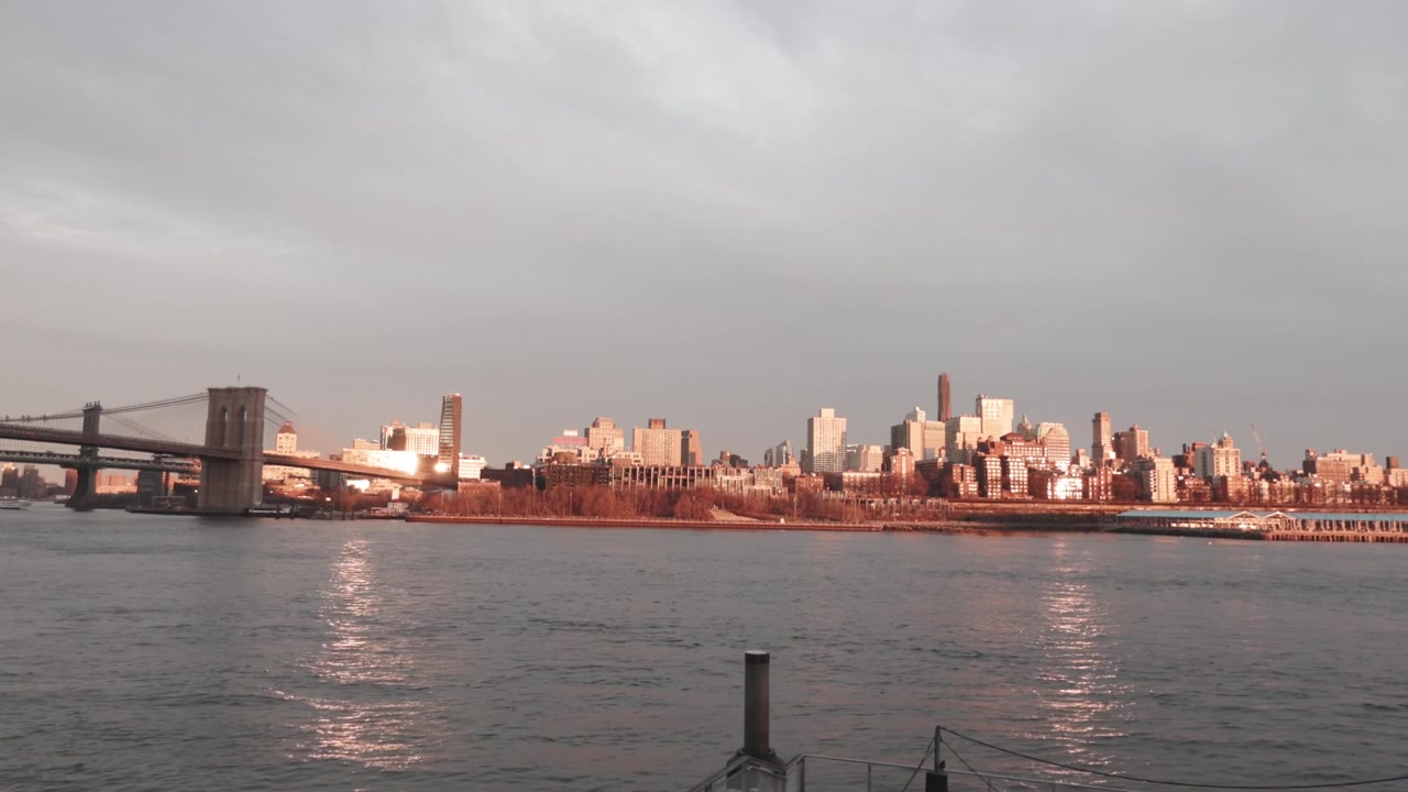 Il Ponte di Brooklyn si estende sul fiume con lo skyline di Manhattan sullo sfondo, che risplende nella calda luce della sera. Ideale per progetti di paesaggio urbano o articoli di viaggio.