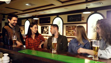 group of friends are sitting at bar counter and talking. beer glasses and bottles, tables are visible. friendly informal atmosphere.