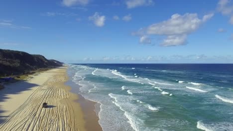 Beautiful-cinematic-descending-shot-over-the-beach-of-Fraser-Island-as-a-solitary-four-wheel-drive-car-drives-up-the-beach-among-the-many-tracks-left-by-other-vehicles