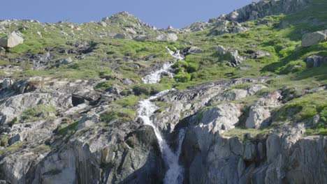 Swiss-Alps-waterfall-from-melting-Rhone-Glacier-ice-flow,-tilting-drone-shot