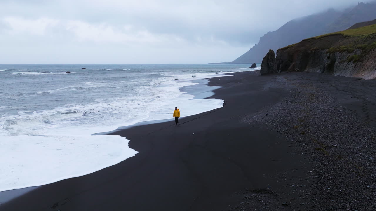 hombre caminando por la costa de la playa de arena negra de lækjavik en islandia