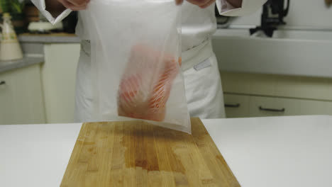 close up shot of male chef putting fresh salmon fillet into airtight bag in kitchen