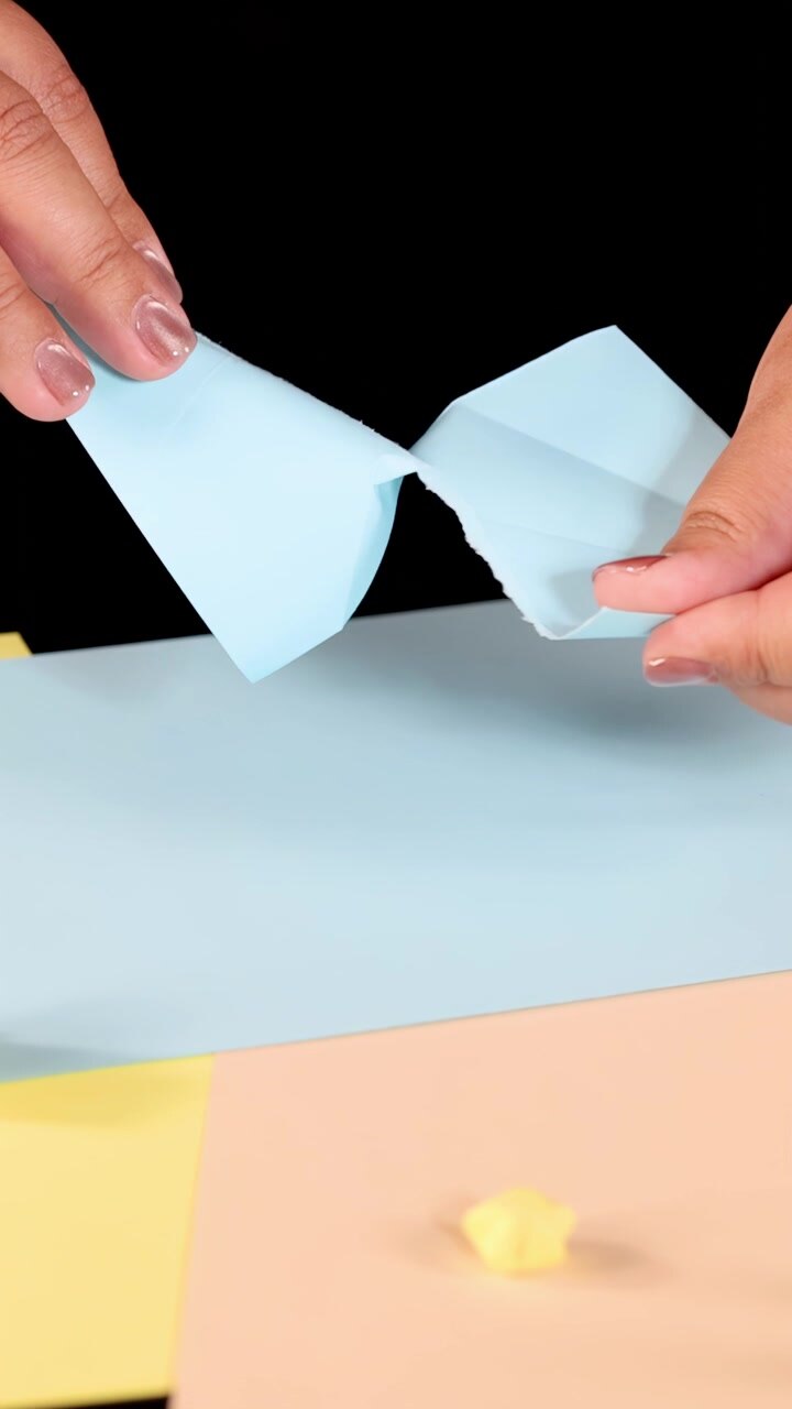 Person tears blue paper by hand on pastel surface under bright, even studio lighting