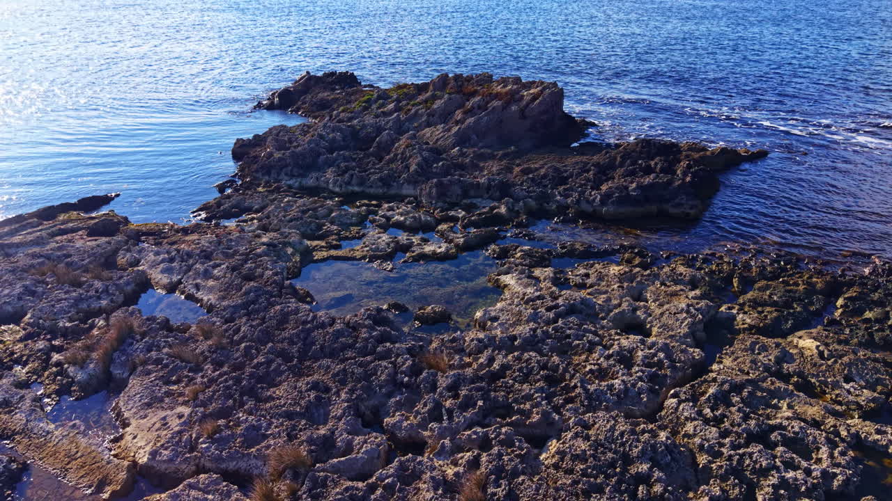 Una vivace formazione rocciosa costiera risplende sotto il sole mentre le onde lambiscono delicatamente i suoi bordi durante una giornata limpida in riva al mare