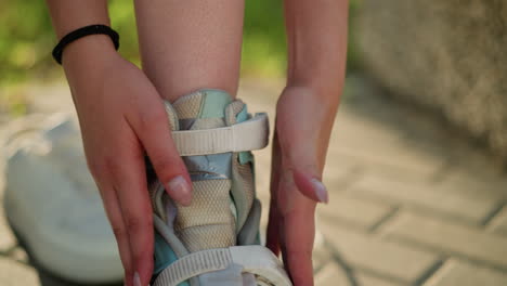 close-up of hands adjusting strap on roller skating shoe under warm sunlight, fingers tightening strap for secure fit, showcasing focus on detail and precision while preparing for outdoor skating