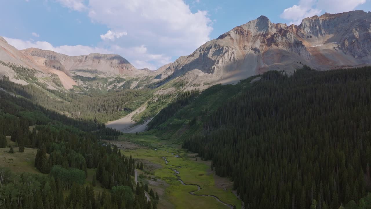 Dòng sông uốn lượn chảy qua một thung lũng núi rộng lớn, dãy núi San Juan của Colorado, cảnh quay kéo lùi trên không