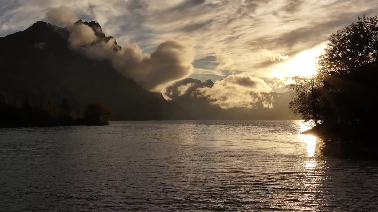 Nascer do sol dourado sobre Walensee com nuvens nebulosas flutuando sobre águas calmas e margens arborizadas