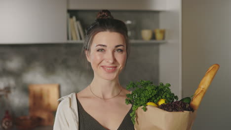 smiling woman holding groceries in kitchen